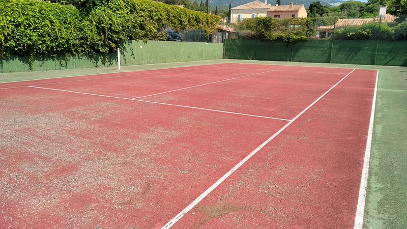 Image de l'état d'un court de tennis en enrobé peint, dégradé et fissuré avant les travaux de rénovation avec le revêtement modulaire. Étape 1